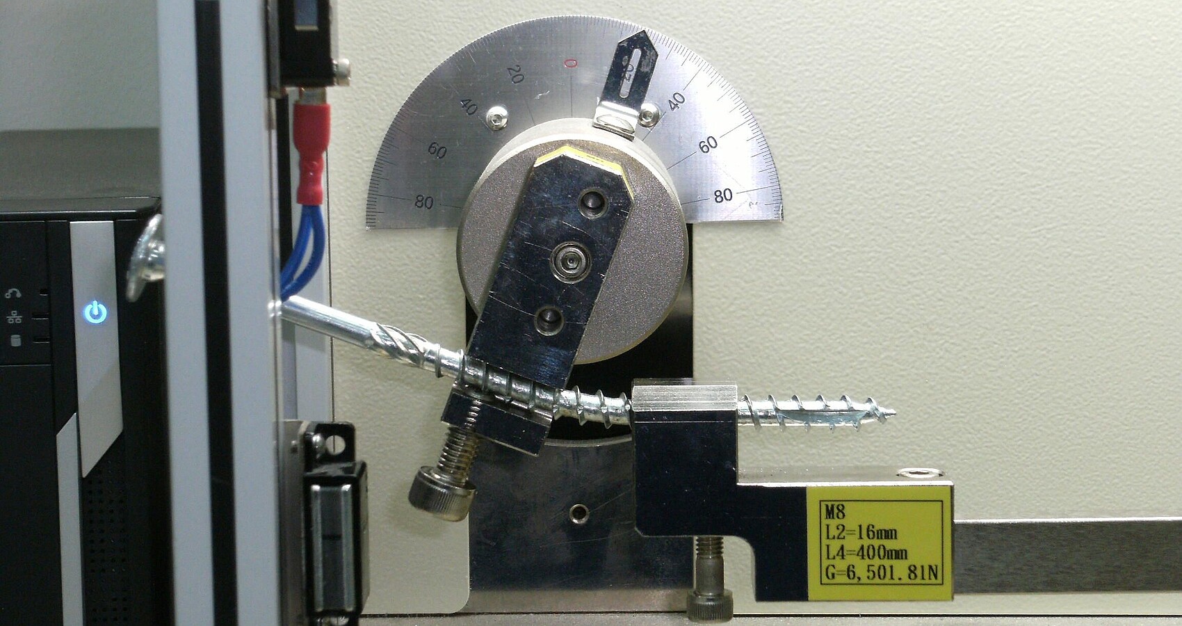 Eine Schraube für den Holzbau wird in einer Biegemaschine geprüft. Wenn die Schraube sich um einen bestimmten Winkel verbiegt, ohne an der Unterseite aufzureißen, hat sie den Test bestanden. 