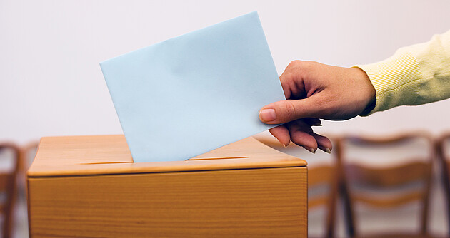 Hand wirft Zettel in Wahlurne