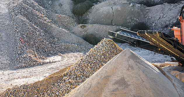 Das Bild zeigt Kiesberge und eine Maschine in einem Steinbruch zum Zerkleinern und Schleifen des Steins