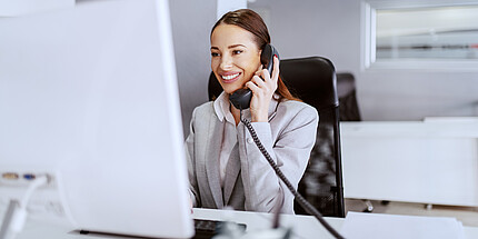 Eine Frau sitzt im Büro am Computer und telefoniert