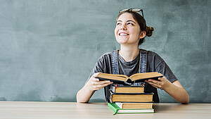 Lächelnde Studentin am Tisch vor einem Bücherstapel