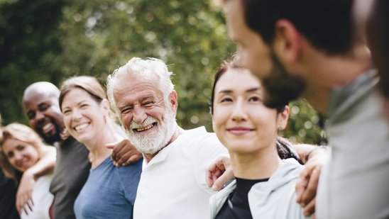 Menschen unterschiedlichen Alters stehen untergehakt in einer Reihe und lachen in die Kamera