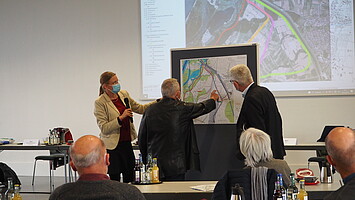 Mehrere Personen diskutieren an einem Plan Trassenvarianten. 