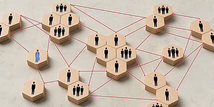 sechseckige gruppierte Holzklötze mit einem, zwei oder drei Menschen drauf, die durch eine rote gestrichelte Linie miteinander verbunden sind