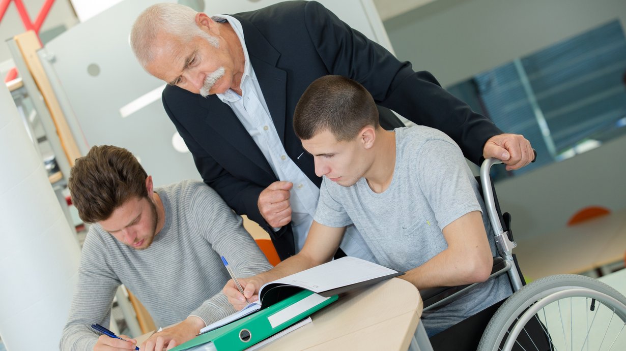 Ein Lehrer beim Unterrichten von zwei Männern, einer im Rollstuhl