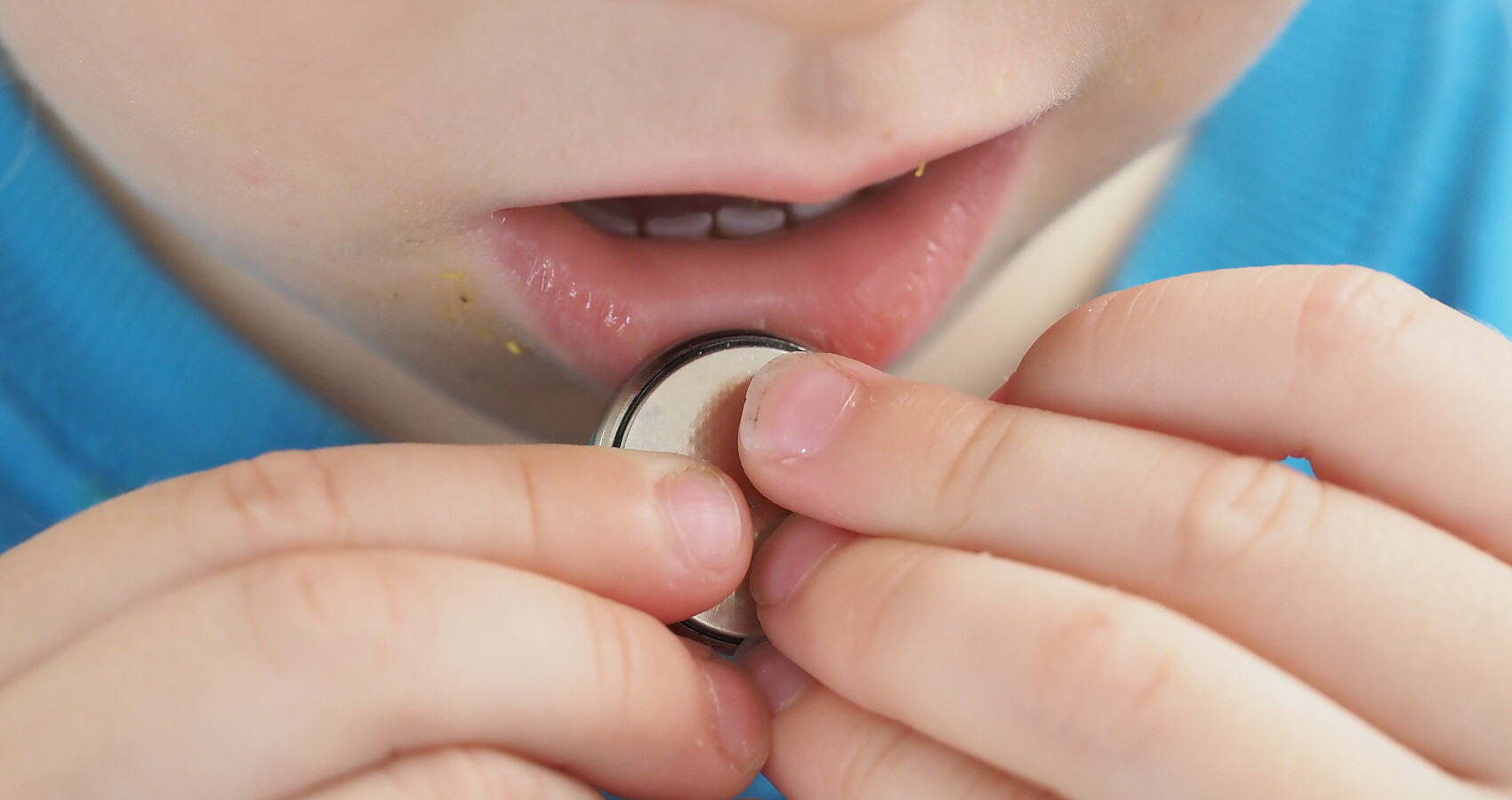 Ein Kind hält eine Knopfzelle in den Händen und führt sie in richtung Mund