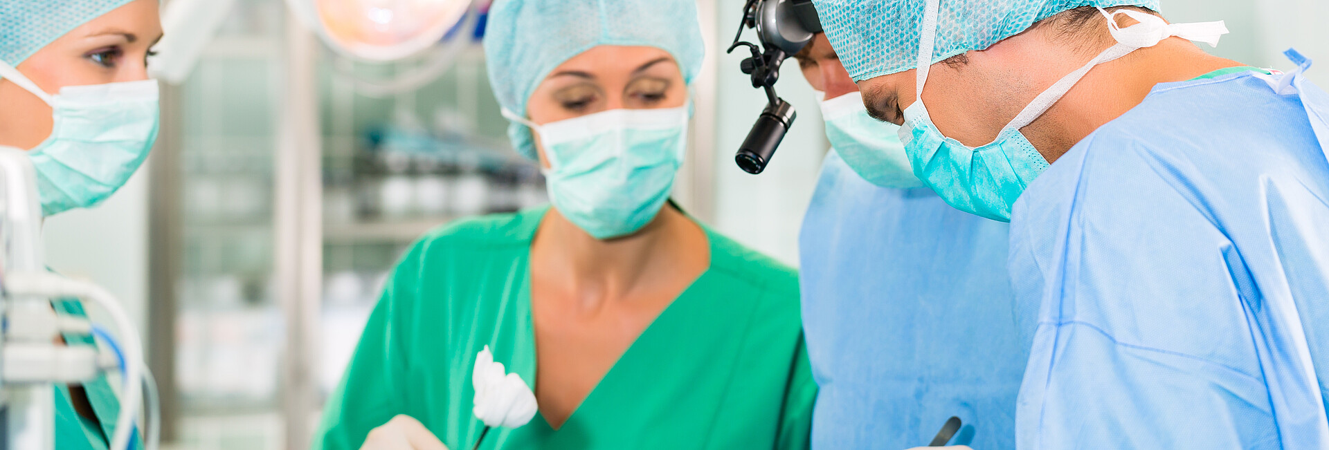 Ärzteteam im OP einer Klinik operiert einen Patienten, eine Assistentin reicht eine Tupferzange