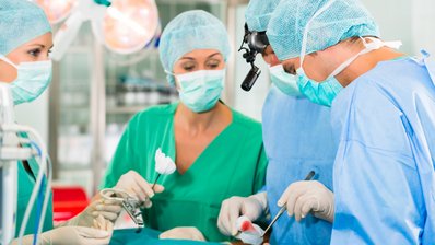 Ärzteteam im OP einer Klinik operiert einen Patienten, eine Assistentin reicht eine Tupferzange