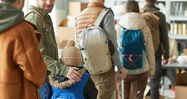 Rückansicht einer Gruppe Flüchtlinge in der Schlange, Fokus auf kleines Kind mit Rucksack