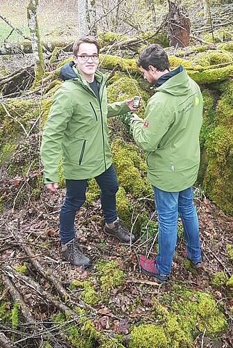Zwei junge Männer stehen im Wald mit einem Smartphone