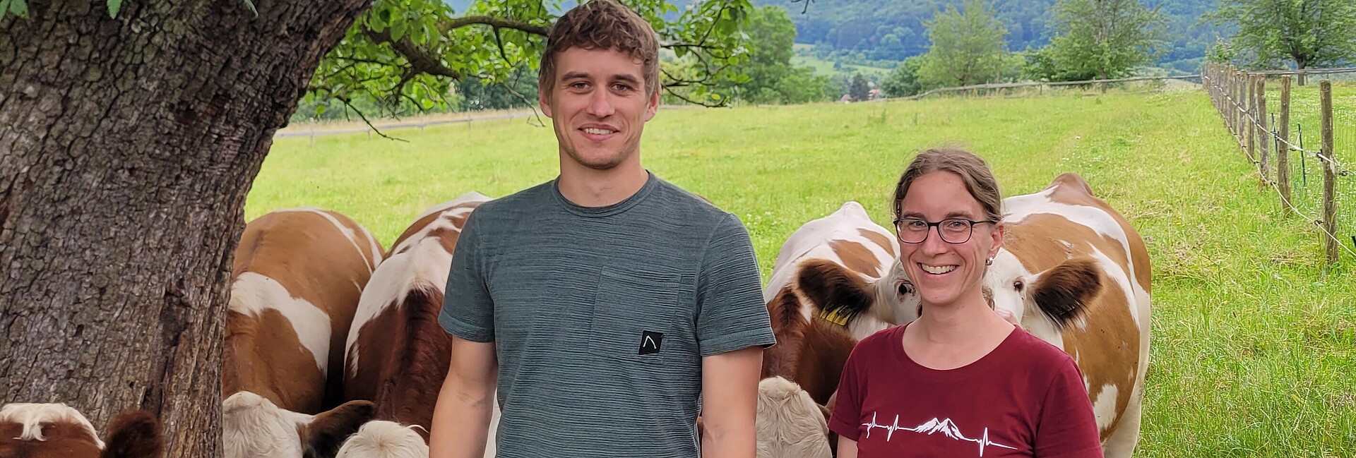 Unter einem Baum stehen Felix Hezel und Dr. Miram Knauer und lächeln in die Kamera. Dahinter stehen Kühe auf der Weide.