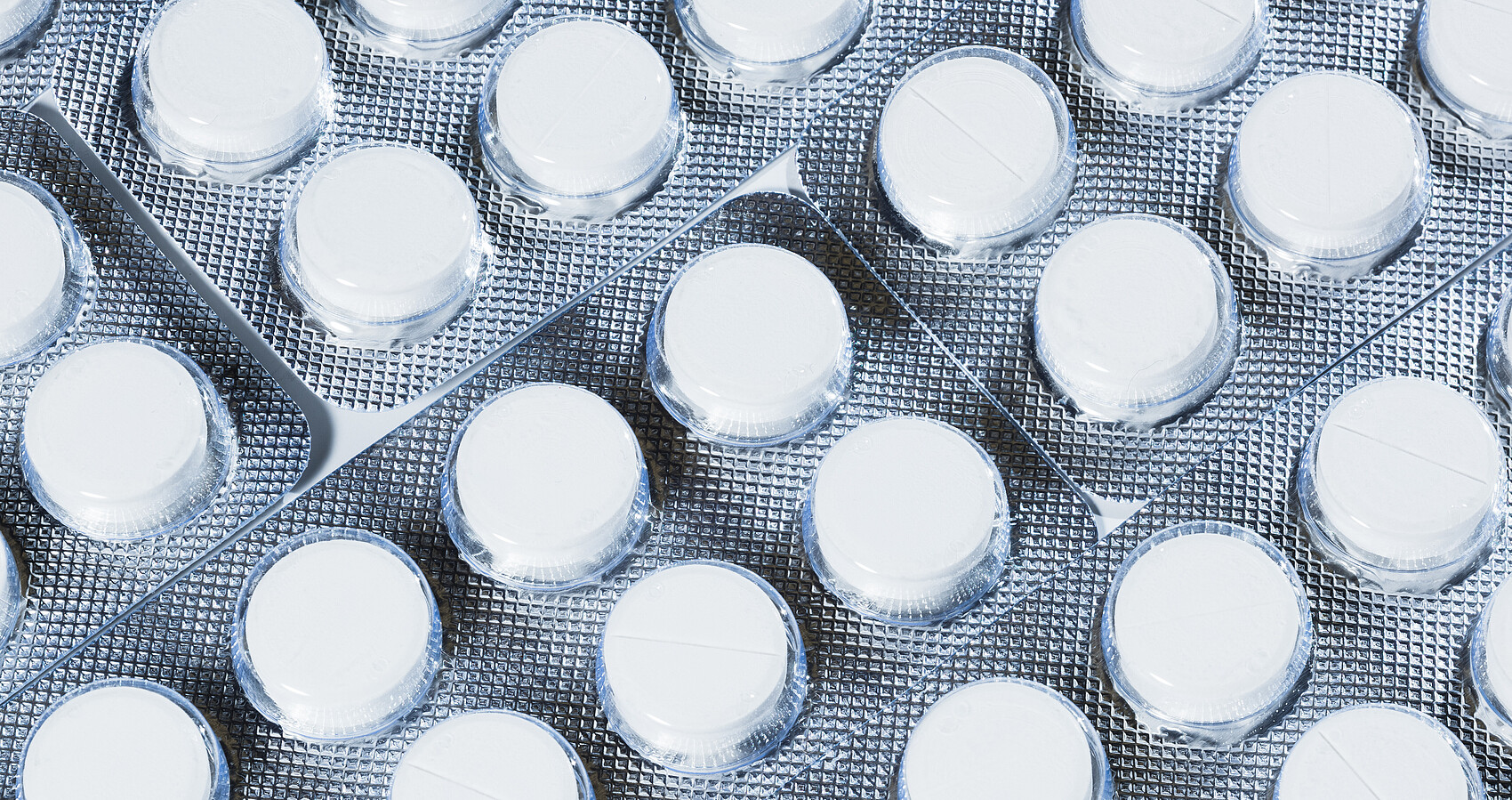 Das Bild zeigt weiße Tabletten in einer Sichtverpackung mit silbernem Hintergrund