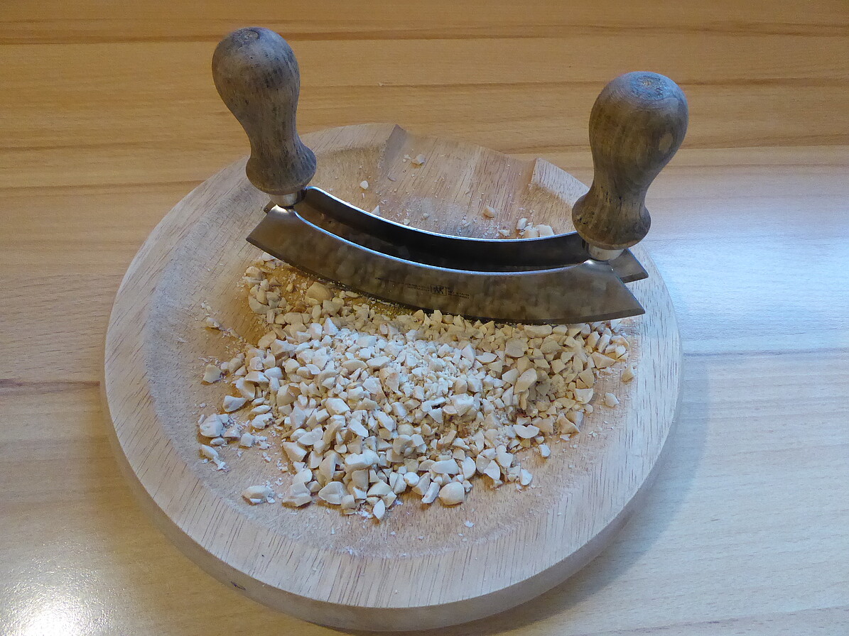 Zerkleinern der Erdnüsse auf einem weißen Teller mit einem Wiegemesser