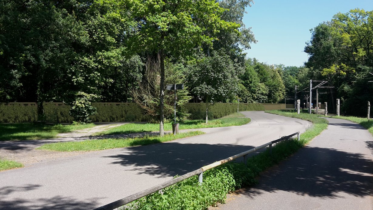 Auf dem Bild sieht man den kurvigen Verlauf der Hermann-Schneider-Allee und den Fußweg im Bereich der Endhaltestelle der Straßenbahn. Dahinter ist als Bildmontage parallel zur Straße die geplante begrünte Spundwand dargestellt.