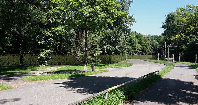 Auf dem Bild sieht man den kurvigen Verlauf der Hermann-Schneider-Allee und den Fußweg im Bereich der Endhaltestelle der Straßenbahn. Dahinter ist als Bildmontage parallel zur Straße die geplante begrünte Spundwand dargestellt.
