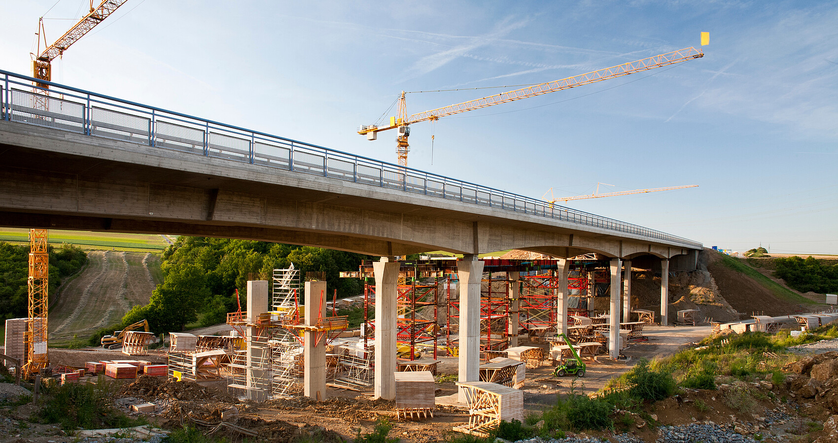 2 Kräne stehen hinter einer Brücke, die saniert werden soll
