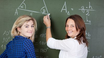 Zwei Mädchen stehen vor einer Tafel mit Formeln