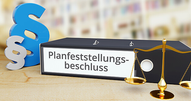 Aktenordner mit Beschriftung Planfeststellungsbeschluss, links daneben ein blaues und ein graues Paragraphenzeichen, rechts eine goldene Waage