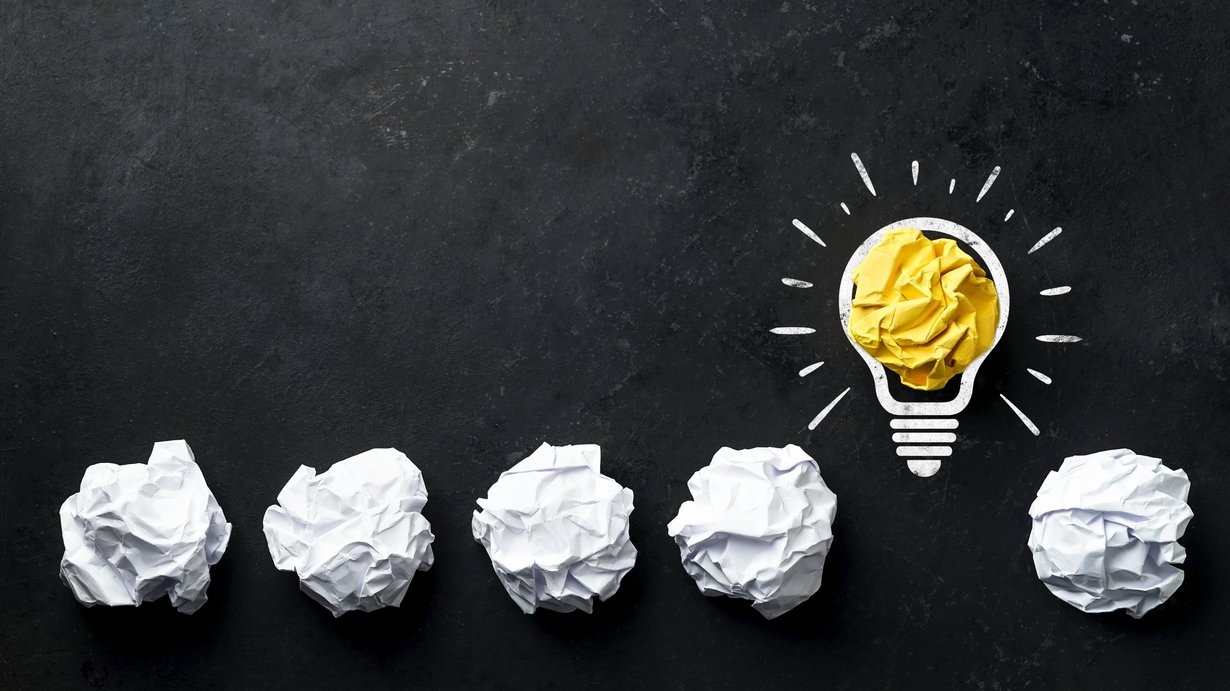 Der Hintergrund ist komplett schwarz. Von links unten an sind am unteren Rand des Bildes vier zusammengeknüllte Stücke weißen Papiers in regelmäßigen Abständen zu sehen, als hätte jemand Ideen aufgeschrieben und wieder verworfen. Nach dem vierten zusammengeknüllten Stück Papier ist eine gezeichnete Glühbirne mit Strahlen zu sehen, in deren Mitte ein gelb leuchtendes zusammengeknülltes Stück Papier zu sehen ist. Um die Glühbirne sind Striche zu sehen, die sich streuendes Licht symbolisieren sollen. Nach der Glühbirne ist wiederum ein zusammengeknülltes weißes Stück Papier im rechten unteren Rand des Bildes zu sehen. 