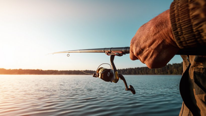 Hände eines Mannes halten eine Angelrute, ein Fischer fängt Fische im Morgengrauen.
