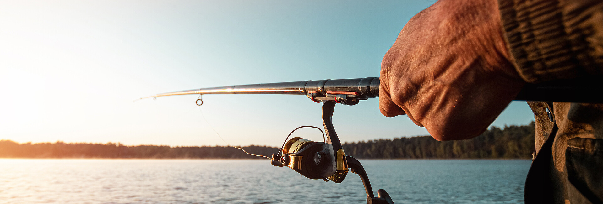 Hände eines Mannes halten eine Angelrute, ein Fischer fängt Fische im Morgengrauen.