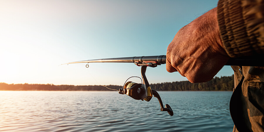 Hände eines Mannes halten eine Angelrute, ein Fischer fängt Fische im Morgengrauen.
