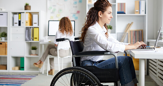 Bild zeigt Frau im Rollstuhl die im Büro am Laptop arbeitet