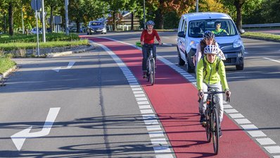 Radfahrer auf einem rot gekennzeichneten Radweg, im Hintergrund ein Auto