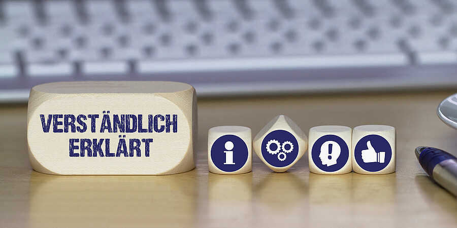 Symbolbild einfach erklärt Verschiedene Würfel mit Symbolen und einer mit der Aufschrift einfach erklärt