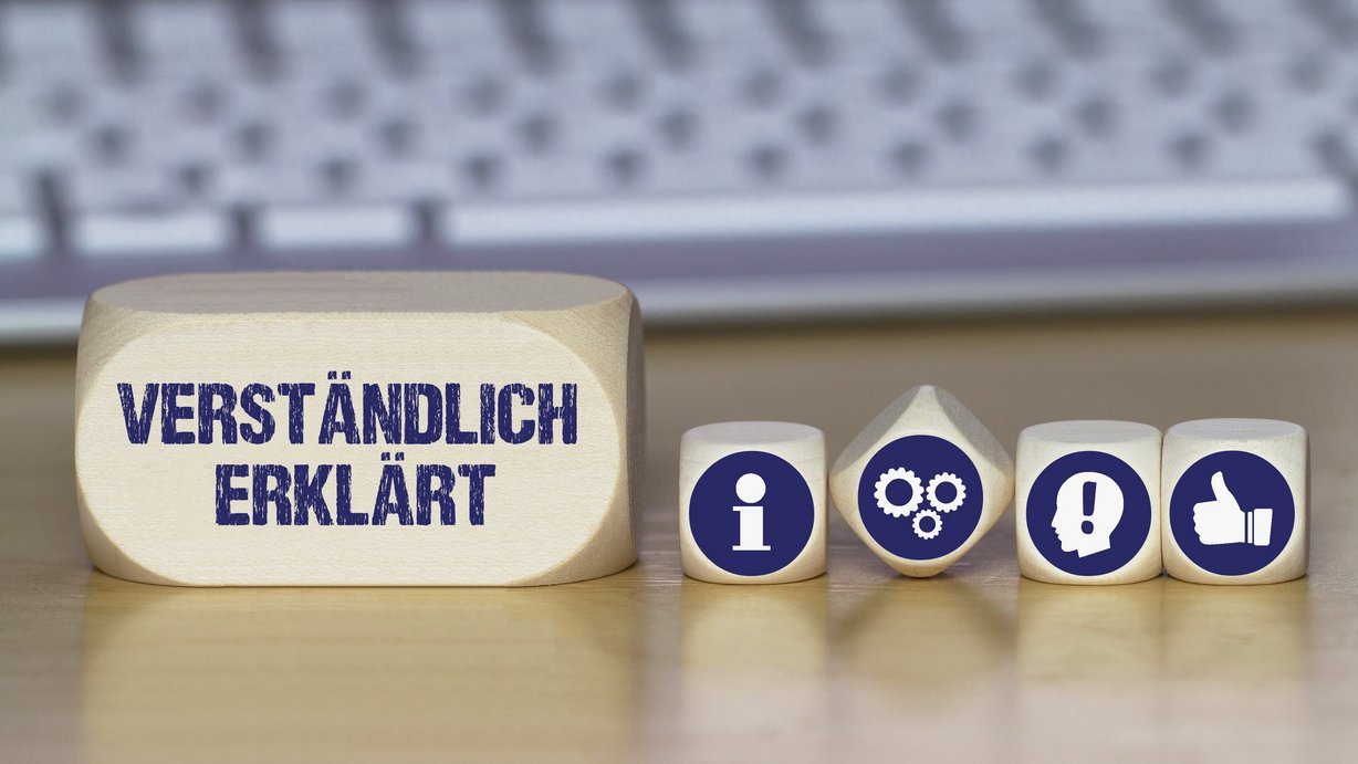 Verschiedene Würfel mit Symbolen und einer mit der Aufschrift einfach erklärt