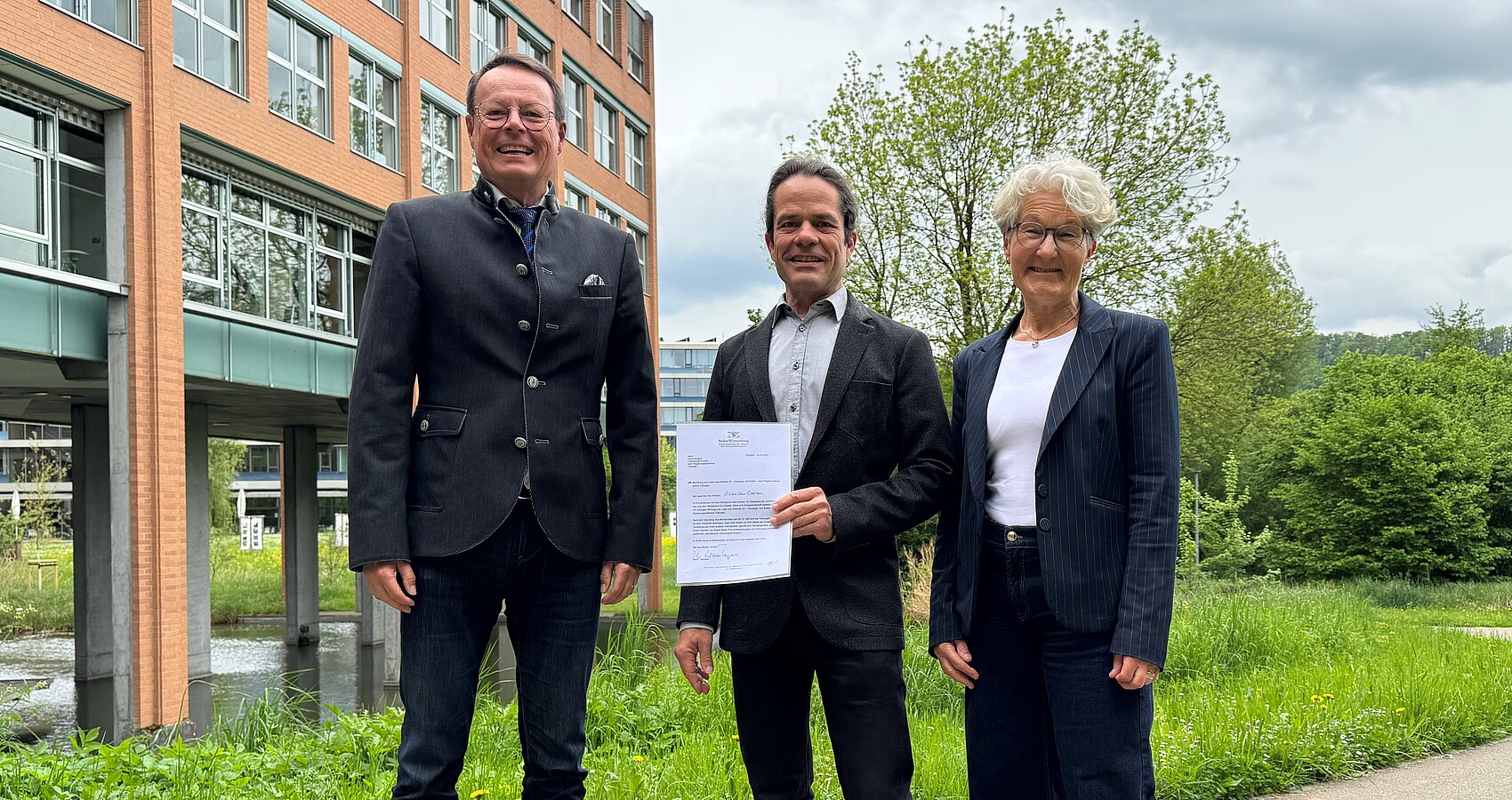 Das Foto zeigt Regierungspräsident Klaus Tappeser, Frank Wolters und Abteilungsleiterin Andrea Bär vor dem Gebäude des RP Tübingen. Herr Wolters hält seine Urkunde in den Händen