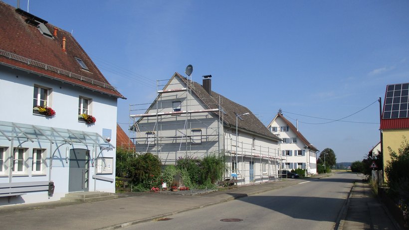 Blick auf eine Straße mit drei Gbeäuden, von denen eines gerade saniert wird.