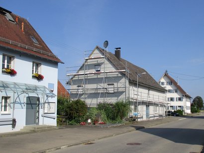 Blick auf eine Straße mit drei Gbeäuden, von denen eines gerade saniert wird.