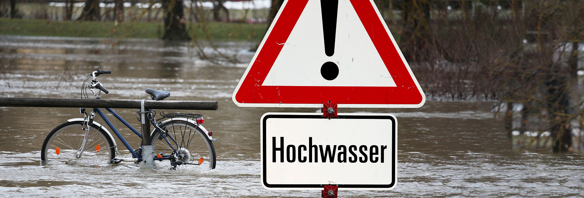 Bild zeigt Hochwasser-Warnschild mit überfluteter Fläche im Hintegrund