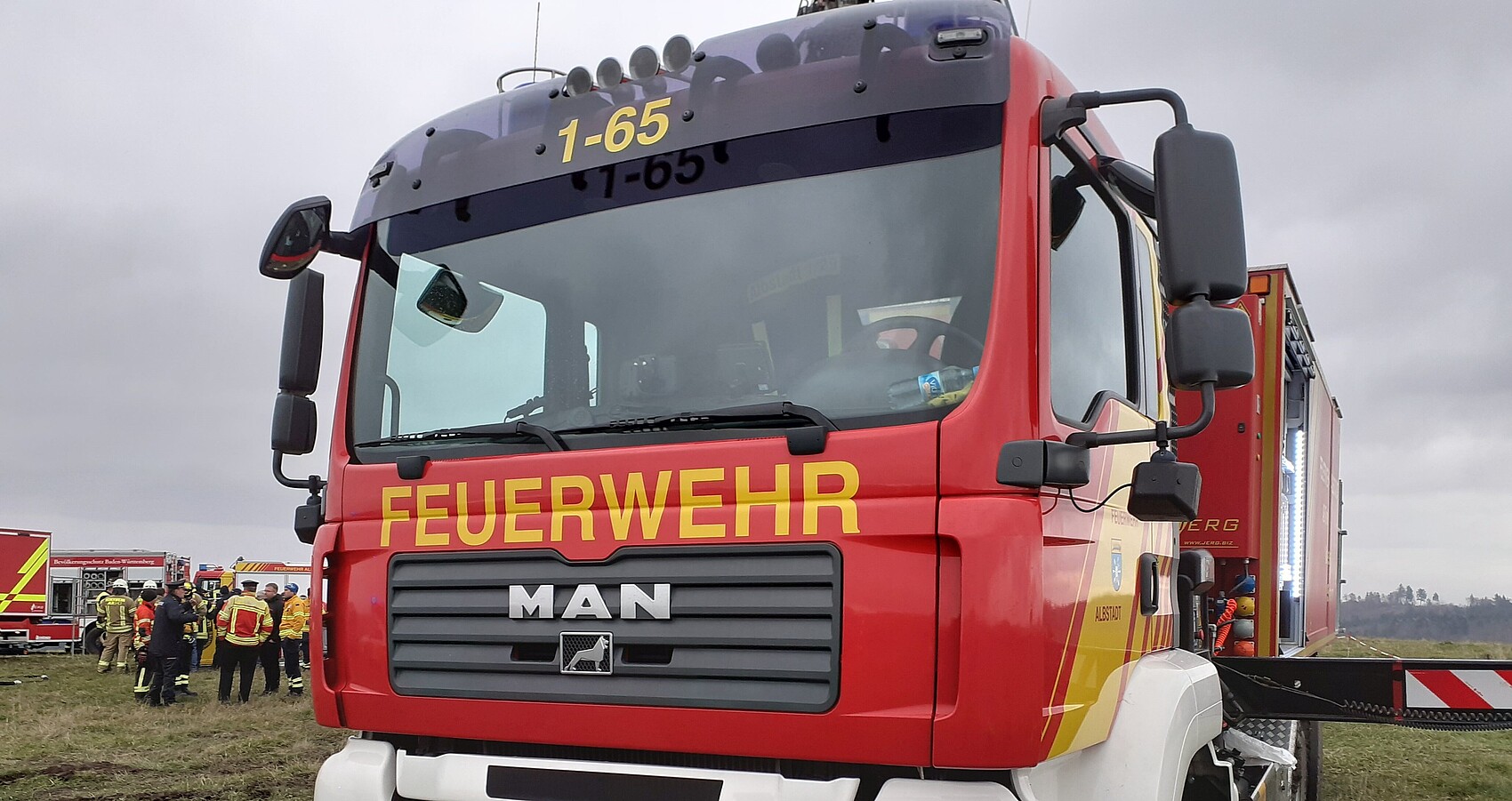 Das Bild zeigt ein rotes Feuerwehrfahrzeug im Gelände bei einer Übung