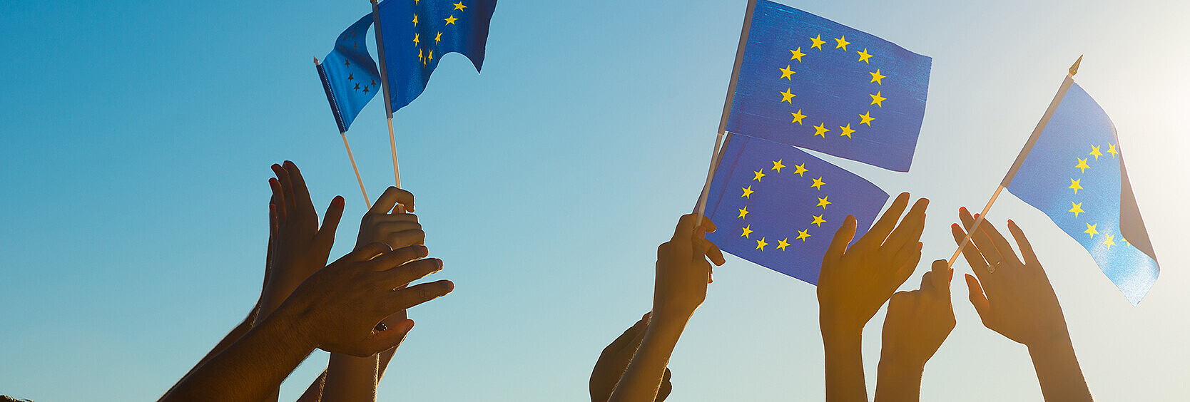 Erhobene Hände, die kleine Flaggen der europäischen Union schwenken