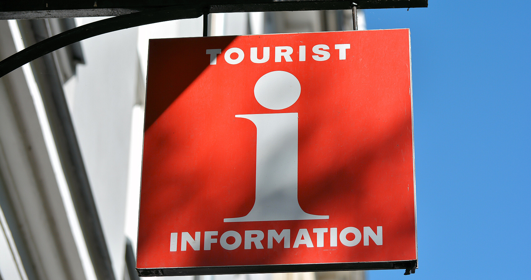 Rotes Schild an Hauswand mit weißem "i" in der Mitte oben "Tourist" unten "Information"