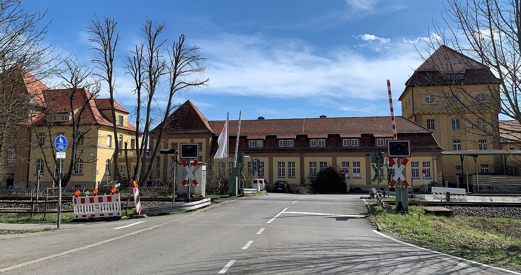 Man blickt auf einen Bahnübergang mit geöffneten Schranken; dahinter sieht man das Bahnbetriebswerk in Tübingen