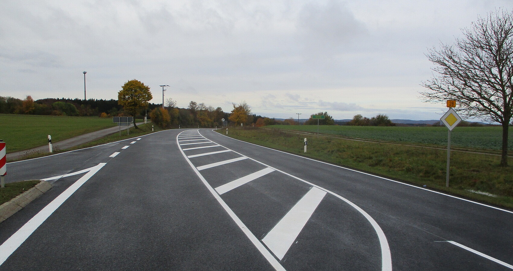 Das Foto zeigt B 28 in Römerstein-Böhringen. Straßenmarkierung und eine Ausfahrt auf der Gegenfahrbahn. Wiesen und Felder an der Seite