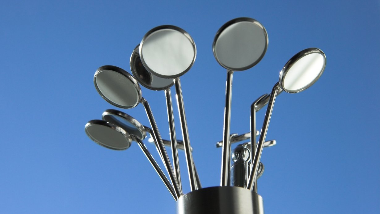 Bild zeigt mehrere Dentalspiegel in einem Behälter vor blauem Hintergrund