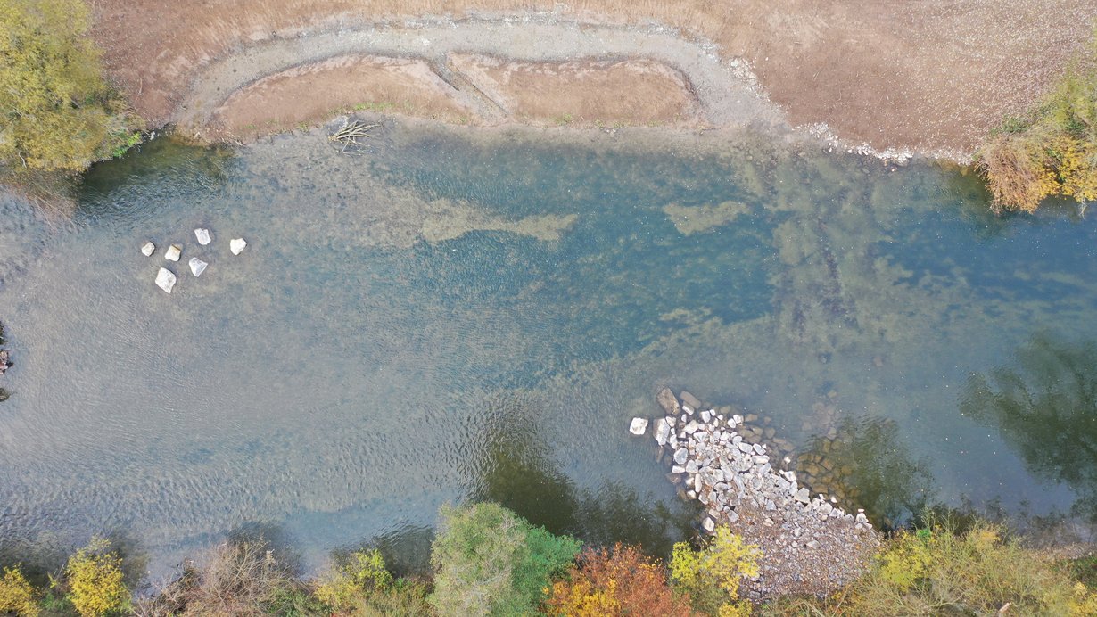 Blick von oben auf den Neckar während der BaupgHase. Man sieht einen blauen Fluss sowie die Ufer mit Kies- und Erdflächen und Gebüsche.
