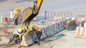 Bauarbeiter an einem Betonstück mit Überstützung eines Baggers