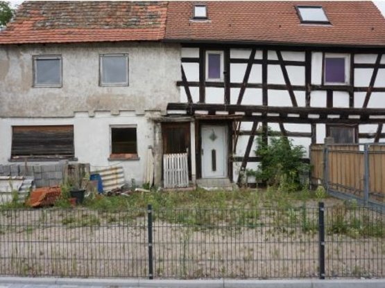 Das Bild zeigt ein Fachwerkhaus, an das noch ein Hinterhaus angebaut ist. Vor dem Hinterhaus liegen Baumaterialien. 