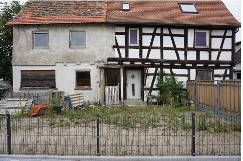 Das Bild zeigt ein Fachwerkhaus, an das noch ein Hinterhaus angebaut ist. Vor dem Hinterhaus liegen Baumaterialien. 