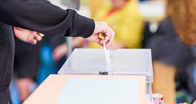 Das Foto zeigt eine Person, die einen Umschlag in eine Wahlurne steckt