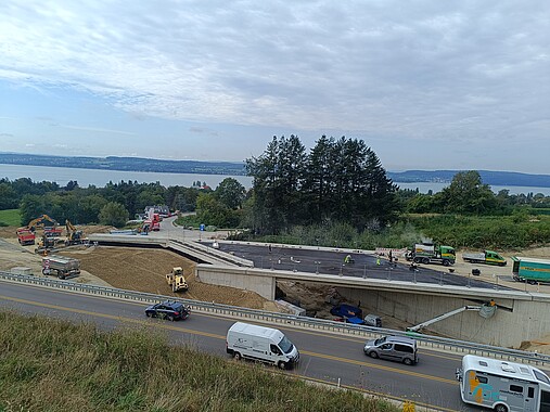 Das Bild zeigt die neue Brücke. Auf der Brücke wird gearbeitet, am Anfang und am Ende ist die Straße noch nicht ganz angebaut. 