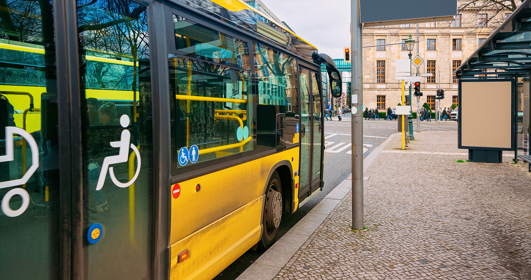 Gelber Bus mit barrierefreiem Einstieg hält an einer Bushaltestelle
