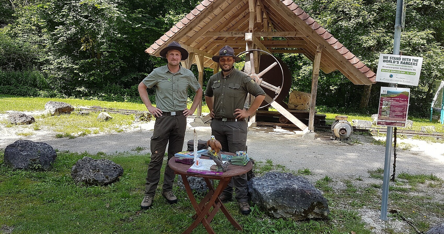 Zwei Ranger Stehen vor einer Holzüberdachung im Wald.