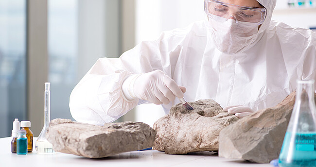 Eine Frau in Schutzkleidung untersucht Gesteinsarten im Labor