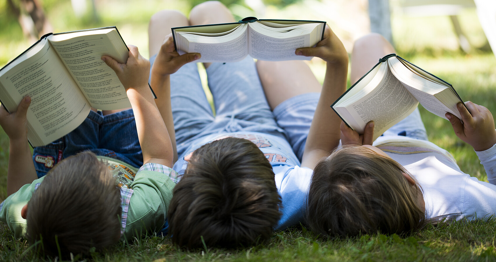 Drei Kinder liegen im Gras und lesen